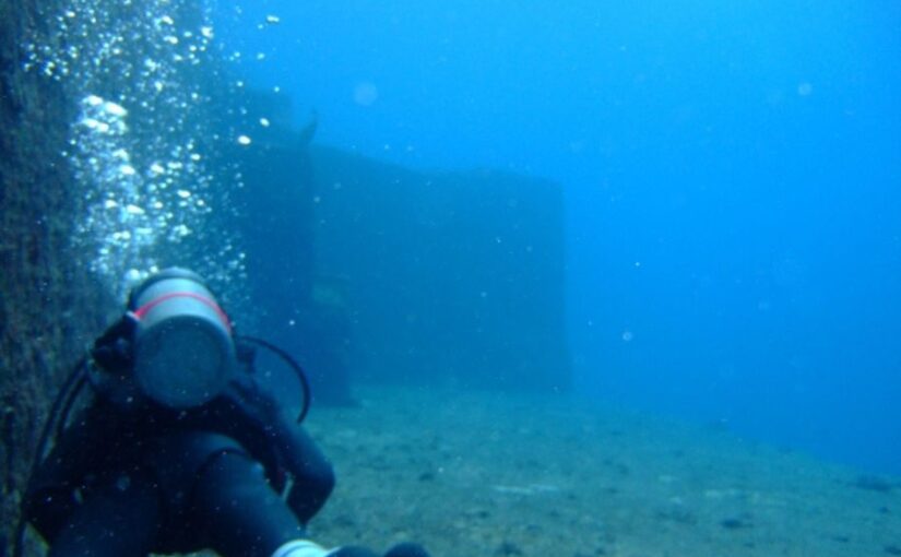 与那国島の海底遺跡で、巨大な岩壁のそばを泳ぐダイバーと湧き上がる泡