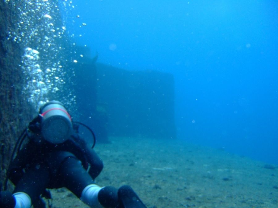 与那国島の海底遺跡で、巨大な岩壁のそばを泳ぐダイバーと湧き上がる泡