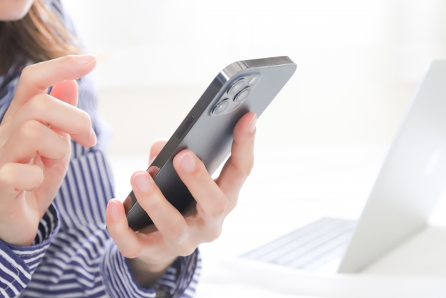 カフェでスマートフォンを操作する女性。手元にはノートパソコンもあり、旅先でのワークスタイルの様子。